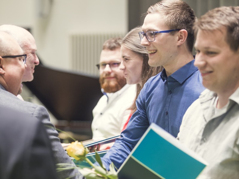 Absolvent:innen nehmen freudig ihre Abschlussurkunden von Professoren entgegen.