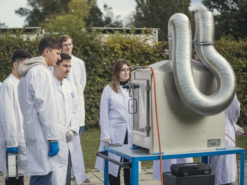 Studierende stehen draußen in Kitteln vor einer Maschine für ihr Projektvorhaben.