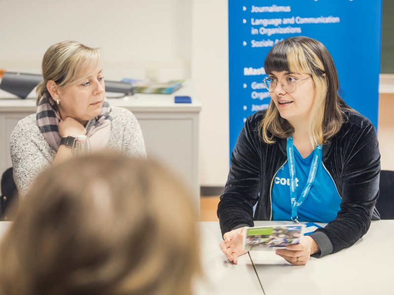 Hochschul-Scout informiert Interessierte zur Studien- und Berufswahl an einem Tisch.