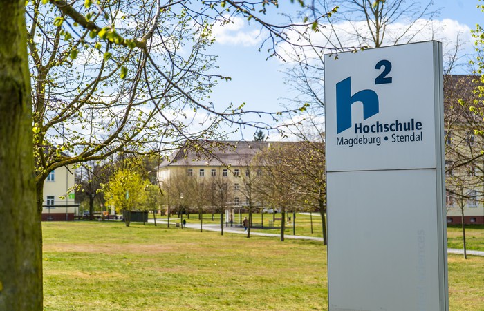 Foto des Hochschulcampus mit dem Schild und Hochschullogo.