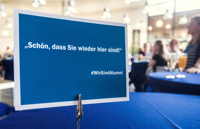Alumni-Veranstaltung mit Besuchern und dem Schild "Schön, dass Sie wieder hier sind!".