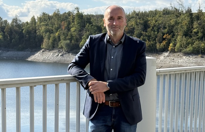 Foto von Absolvent Mario Hohmann am Geländer einer Brücke über dem Fluss.