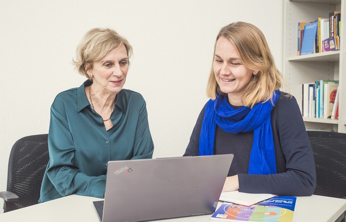 Prof. Dr. Elke Grittmann und Dr. Lina Brink schauen gemeinsam auf einen Laptop.
