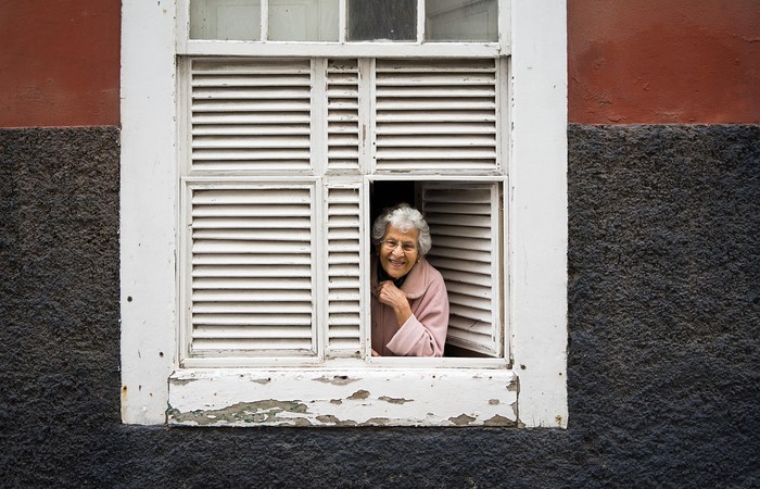 Foto in der eine ältere Dame aus einem Fenster schaut.