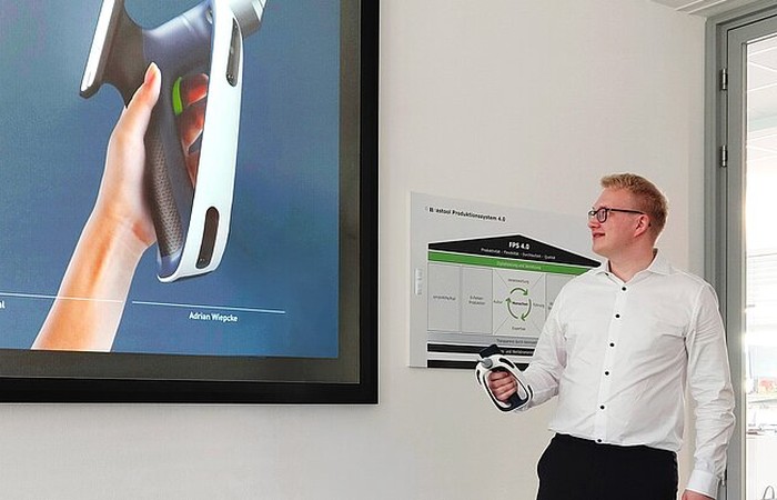 Absolvent Adrian Wiepcke stellt sein Projekt vor mithilfe einer Multimediatafel und dem Produkt.