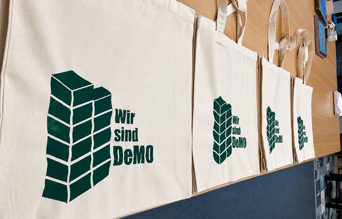 Auslage von Stoffbeuteln auf einem Tisch zum Projekt mit gestapelten Quadern und dem Projektitel als Aufdruck.