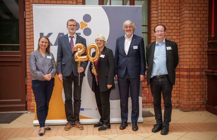KAT-Mitglieder stehen vor einem Banner und zelebrieren das 20. Jubiläum.