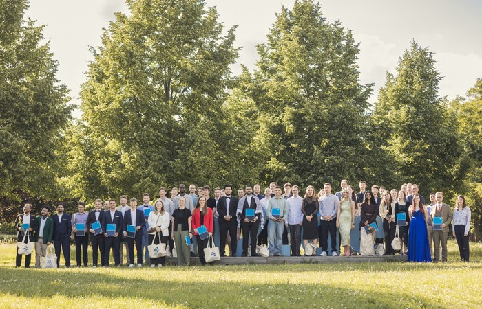 Gruppe von Absolvent:innen im Grünen des Hochschulcampus.