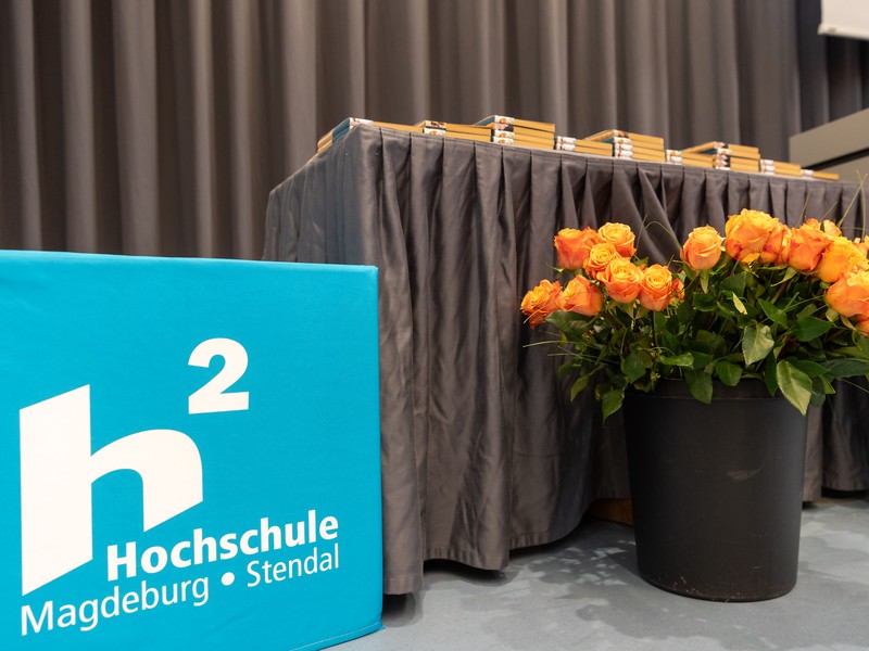 Rosen, Notizblockstapel und das Hochschullogo für die Absolvent:innenfeier.